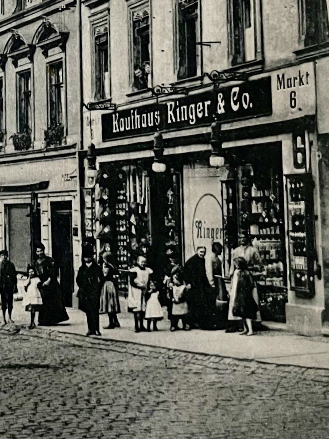 Historic black and white postcard. Depicted is the front of the Ringer & Co. department store at Markt 6 in Werdau. In front of the shop is a queue of people. Two women are looking out of the first-floor window.